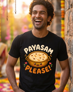 A man wearing a black graphic t-shirt with a cartoon pot of food and the text 'PAYASAM PLEASE!' in a festive, decorated outdoor setting.