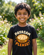 A young boy smiling outdoors wearing a black t-shirt with a cartoon pot of food and the text 'PAYASAM PLEASE!' printed on the front.