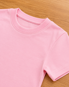 Baby pink  t shirt lie on wooden background which focus of sleeve and neck part.