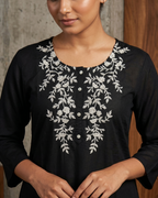 Black top with white floral embroidery worn by a person against a neutral background
