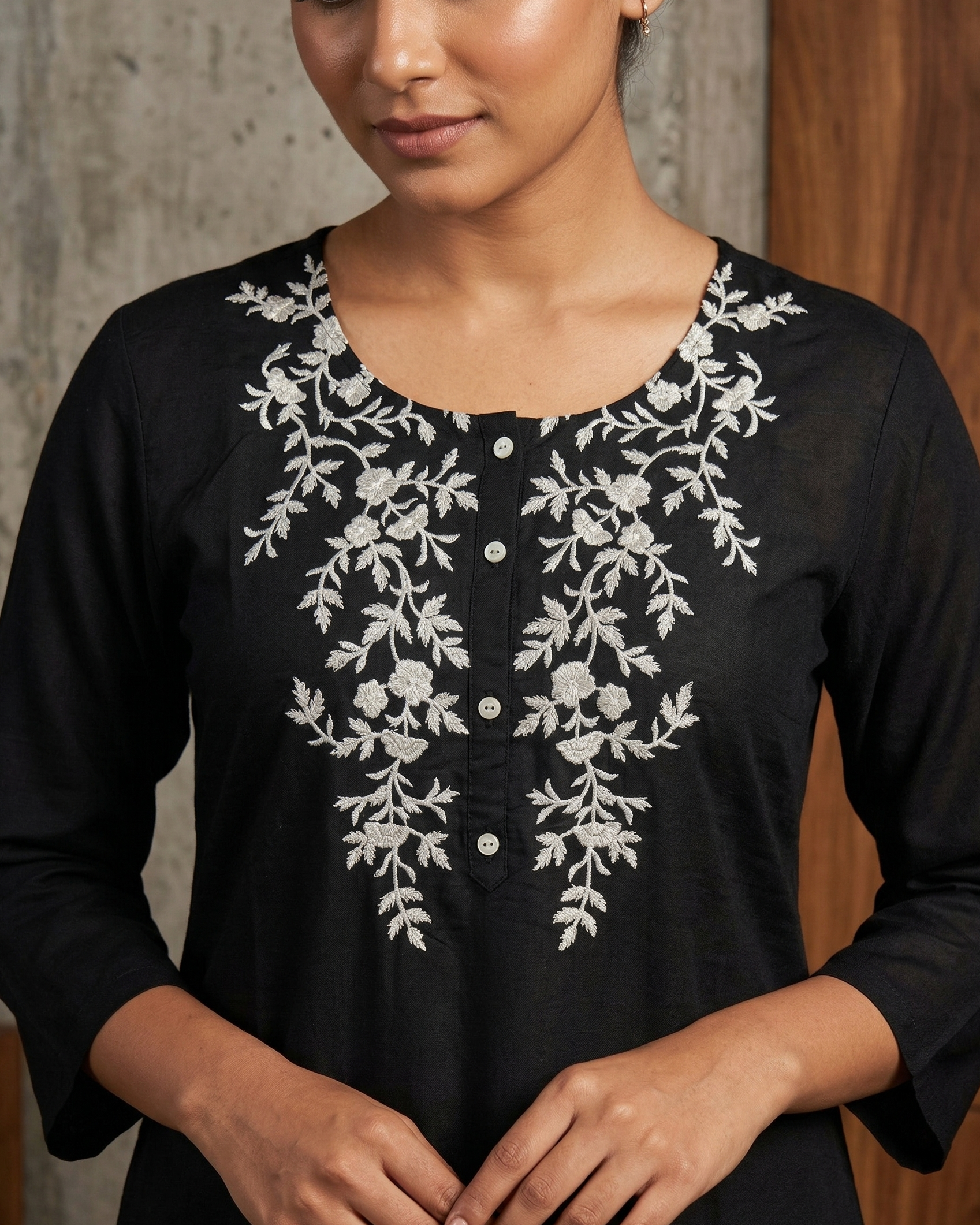 Black top with white floral embroidery worn by a person against a neutral background