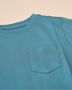 Blue t-shirt with a pocket on a beige background.