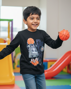 Child holding a basketball in an indoor playground with colorful equipment.
