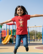 Child in a red shirt with a reindeer graphic jumping on a playground.