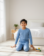 Child in blue checkered pajamas sitting on a bed with toys in a bedroom.