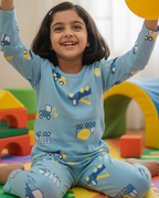 Child in blue pajamas with vehicle pattern playing with a yellow ball on a colorful play mat.