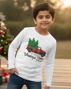 Child wearing a Christmas-themed shirt with a tree and truck graphic, standing in front of a decorated Christmas tree.