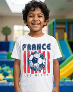 Child wearing a 'France Les Bleus' t-shirt with a soccer ball design in an indoor playground.