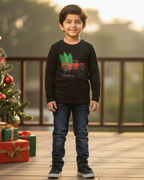 Child wearing a black shirt with a Christmas design, standing in front of a decorated Christmas tree and presents.