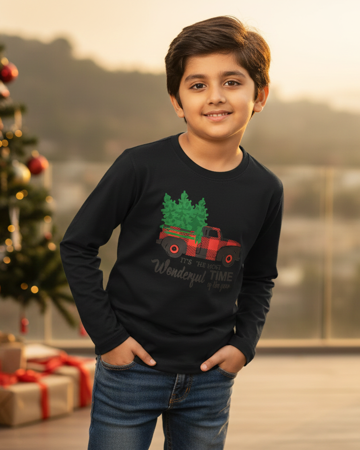 Child wearing a black sweater with a Christmas design, standing in front of a decorated Christmas tree.