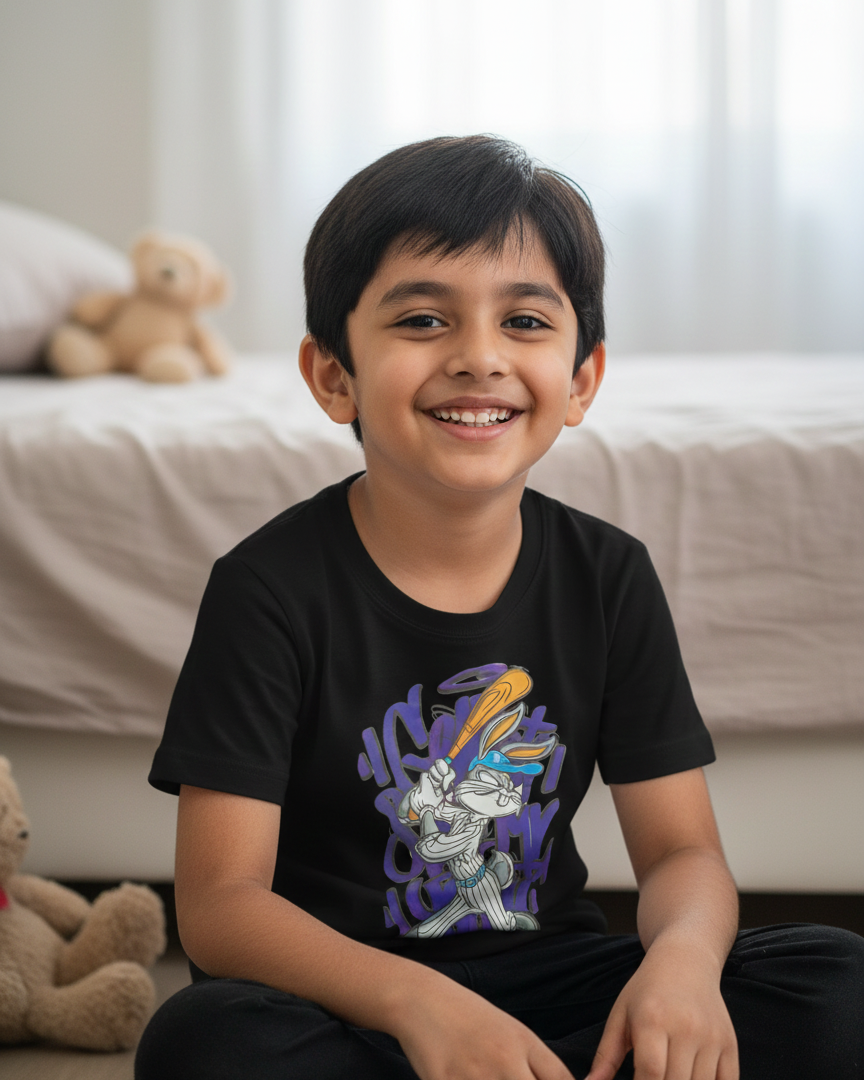 Child wearing a black t-shirt with a colorful graphic design, sitting on a couch with teddy bears.