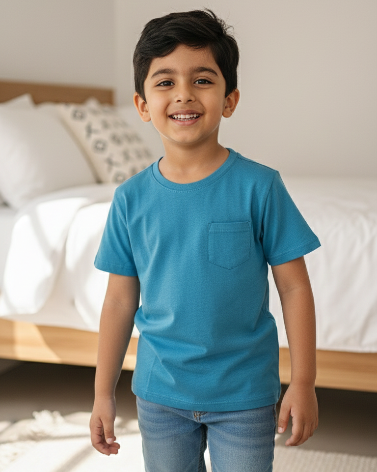 Child wearing a blue t-shirt and jeans standing in a bedroom.