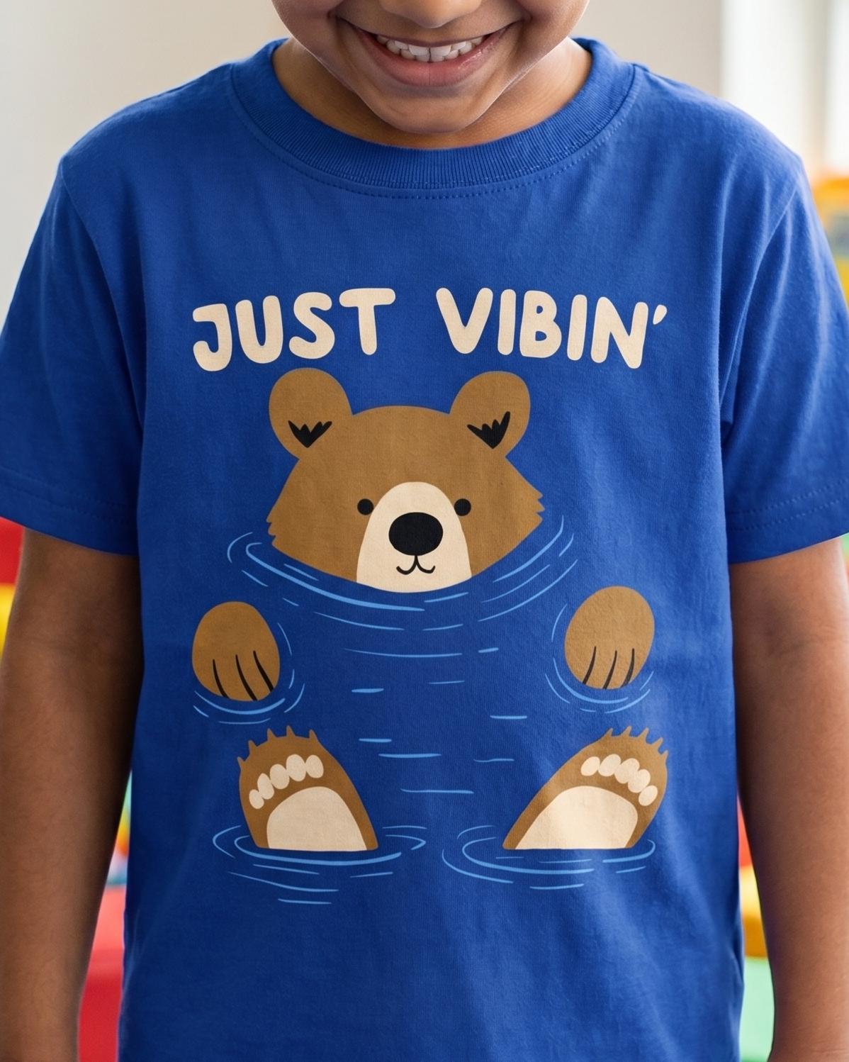 Child wearing a blue t-shirt with a bear graphic and text in a colorful indoor setting