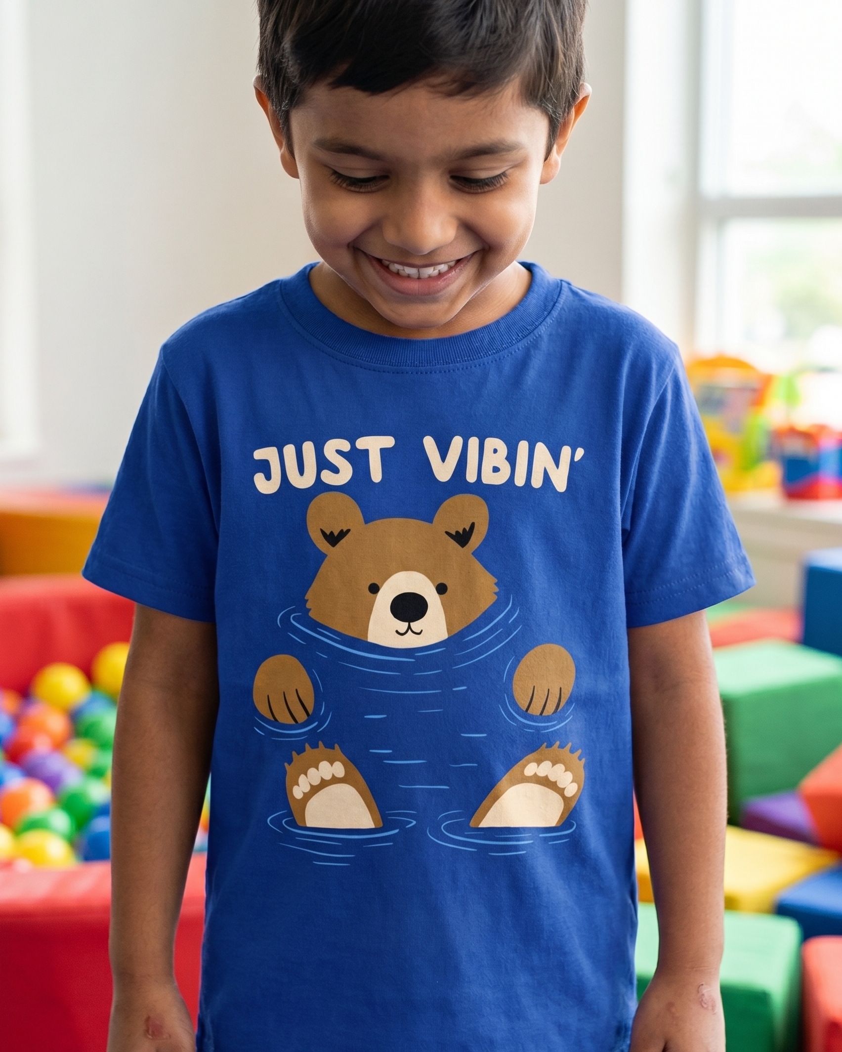 Child wearing a blue t-shirt with a bear graphic and text in a colorful indoor setting