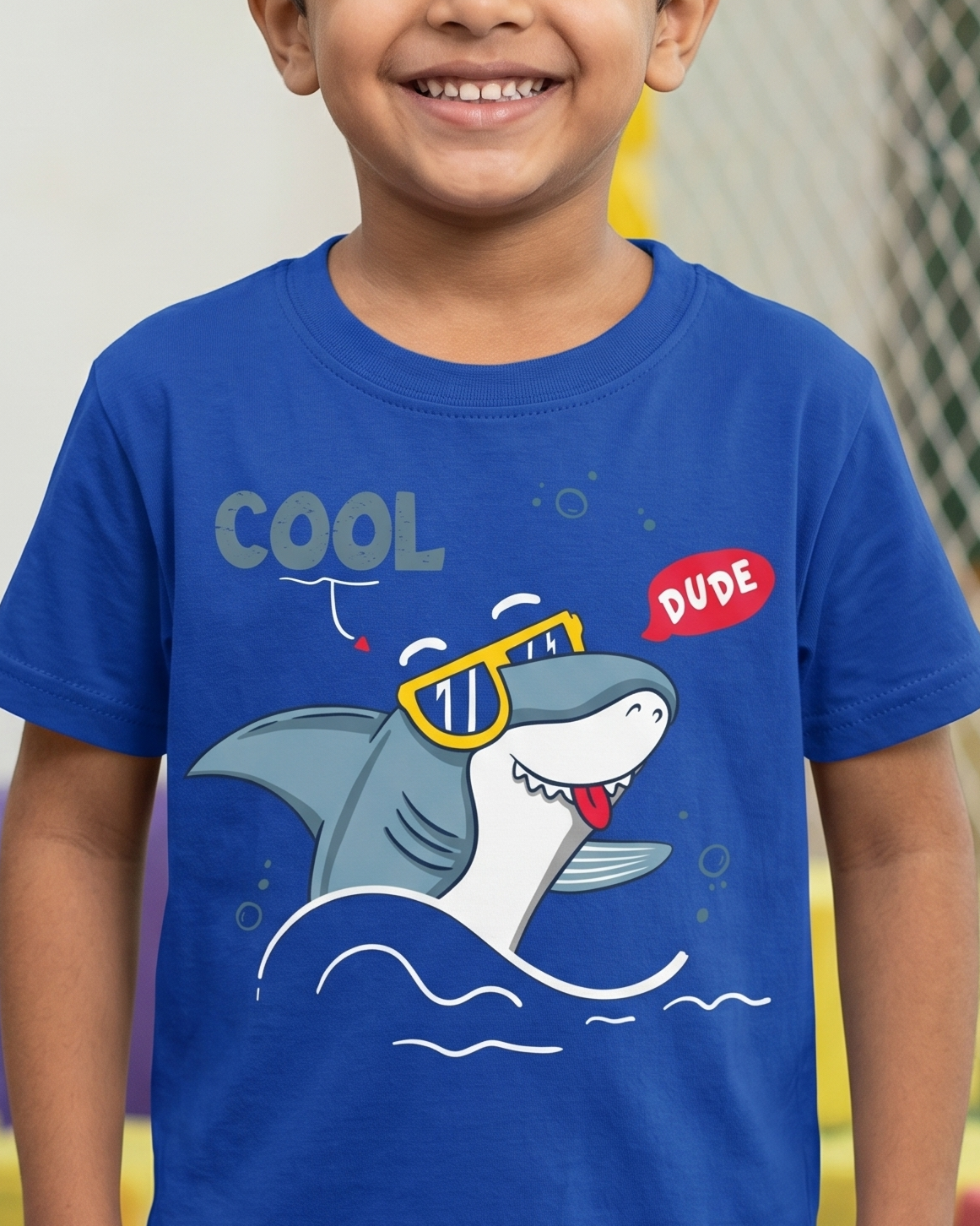 Child wearing a blue t-shirt with a shark graphic and text in a colorful indoor setting