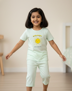Child wearing a light green t-shirt and pants with a smiley face design indoors.