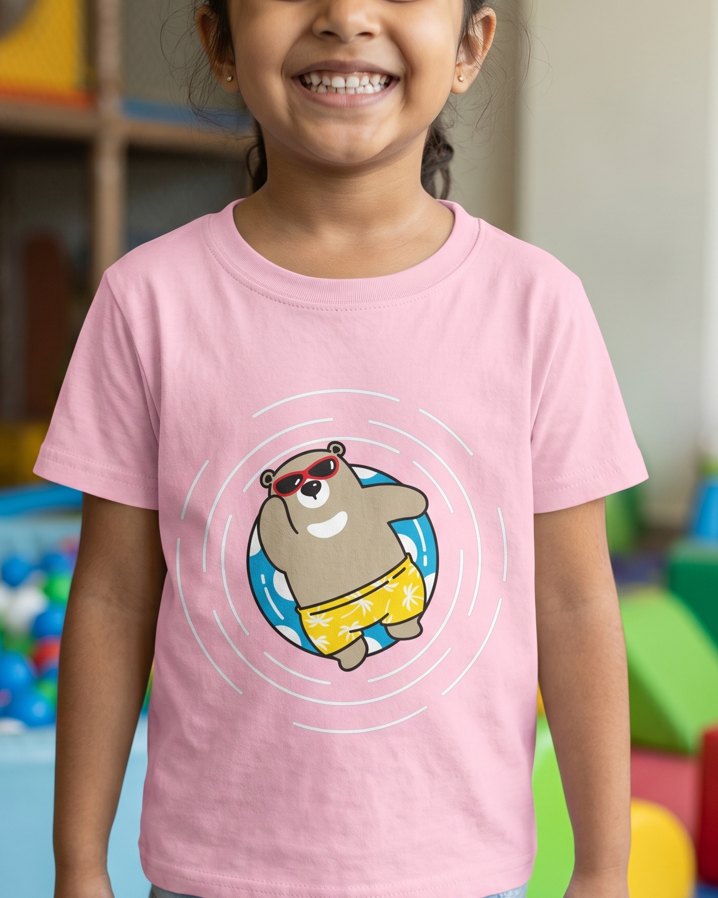 Child wearing a pink t-shirt with a cartoon bear design in a colorful playroom.