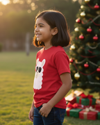 Child wearing a red shirt with a white bunny design, standing in front of a Christmas tree and presents outdoors.