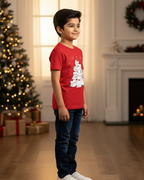 Child wearing a red shirt with a white graphic in a festive room with a Christmas tree and fireplace.