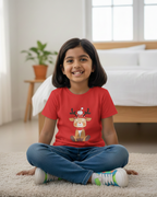 Child wearing a red t-shirt with a reindeer graphic sitting on the floor in a bedroom.