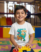 Child wearing a t-shirt with a dinosaur graphic and text, sitting on colorful blocks in a playroom.