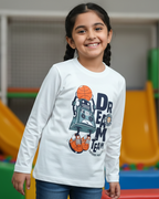 Child wearing a white long-sleeve shirt with a robot and basketball design in an indoor playground.