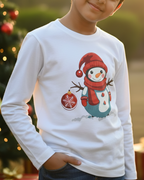 Child wearing a white long-sleeve shirt with a snowman design in front of a Christmas tree.