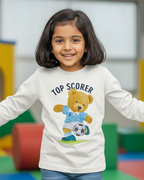 Child wearing a white long-sleeve shirt with a teddy bear graphic and text in an indoor play area.