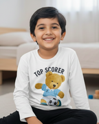 Child wearing a white long-sleeve shirt with a teddy bear graphic and text, sitting on the floor in a room.