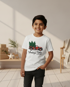 Child wearing a white t-shirt with a Christmas design in a room with a wooden table and chair.