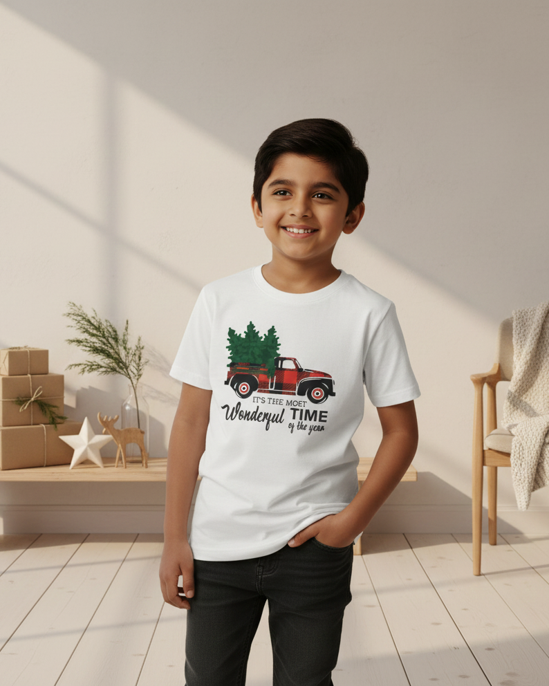 Child wearing a white t-shirt with a Christmas design in a room with a wooden table and chair.