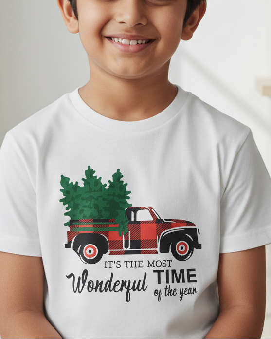 Child wearing a white t-shirt with a Christmas truck graphic and text in a room with decorative items.