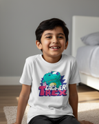 Child wearing a white t-shirt with a dinosaur graphic and text, sitting on the floor.