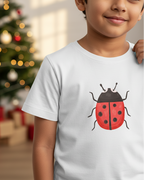 Child wearing a white t-shirt with a ladybug design, Christmas tree in the background