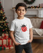 Child wearing a white t-shirt with a ladybug design in a festive room with Christmas decorations.
