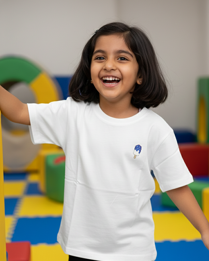 Child wearing a white t-shirt with a small design, standing in a colorful play area.