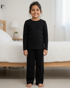 Child wearing black pajamas standing in a bedroom.
