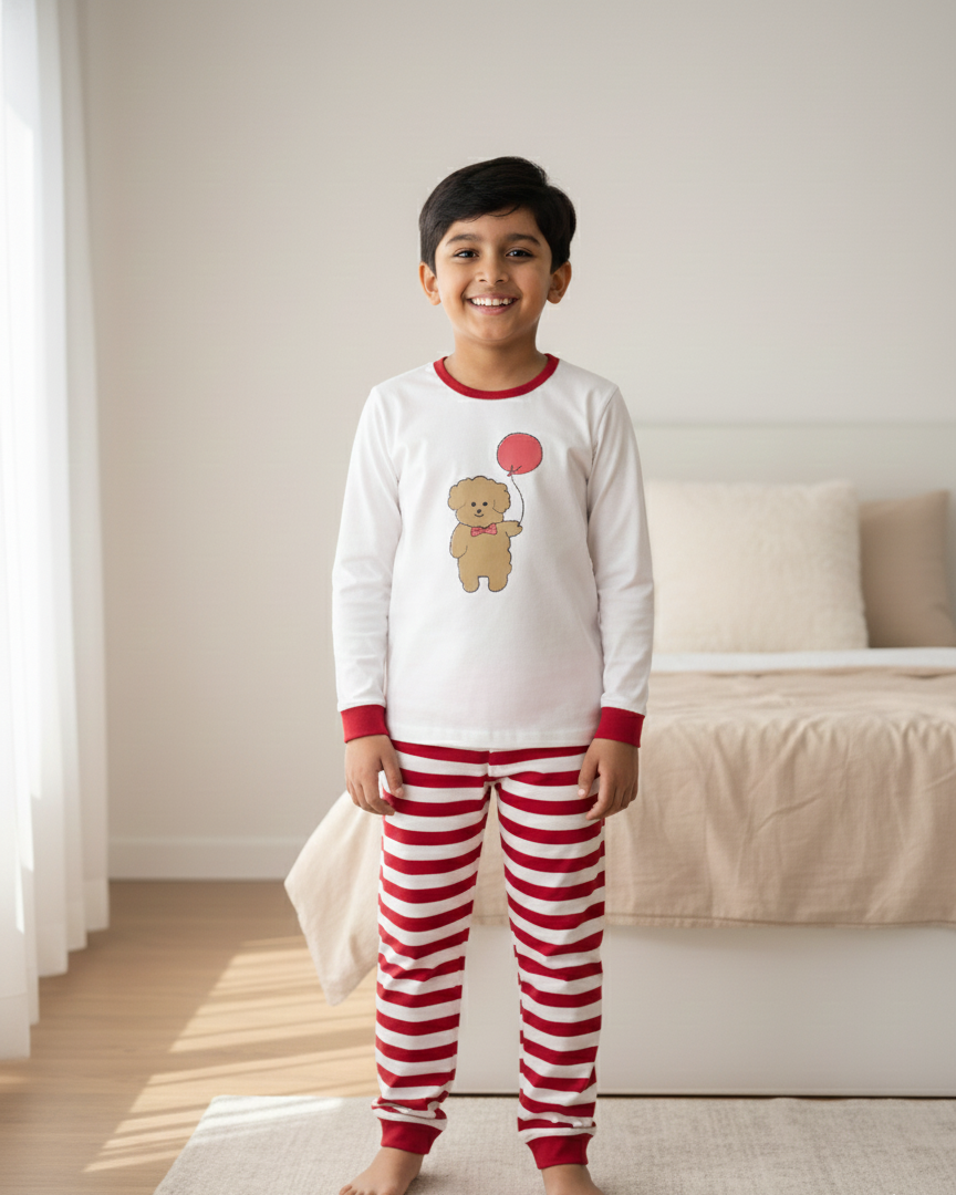 Child wearing red and white striped pajama pants and a matching top with a teddy bear design in a bedroom.