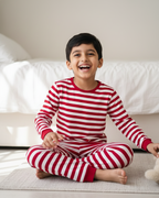 Child wearing red and white striped pajamas sitting on a bed.