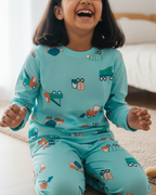 Child wearing teal pajamas with vehicle prints, sitting on a bed.