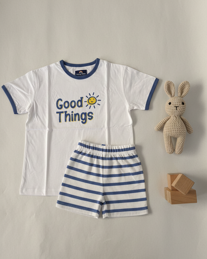 Children's outfit with white t-shirt and striped shorts, accompanied by a plush toy and wooden blocks on a neutral background.
