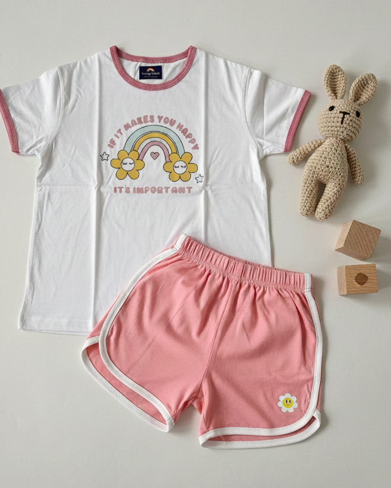 Children's white t-shirt with rainbow and flower design and pink shorts on a light gray background.
