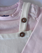 Close-up of a pink shirt with white straps and wooden buttons on a light background