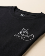 Close view of “Eat, Sleep, Travel, Repeat” embroidered Black Regular Fit T-shirt placed on the Light Beige Background