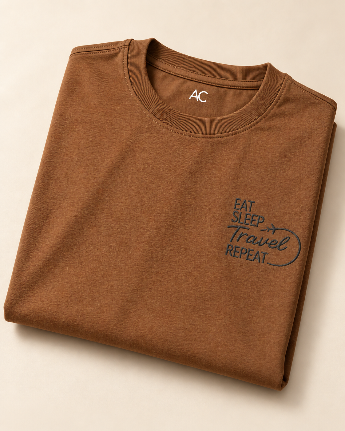 Close view of “Eat, Sleep, Travel, Repeat” embroidered Brown Regular Fit T-shirt placed on the Light Beige Background