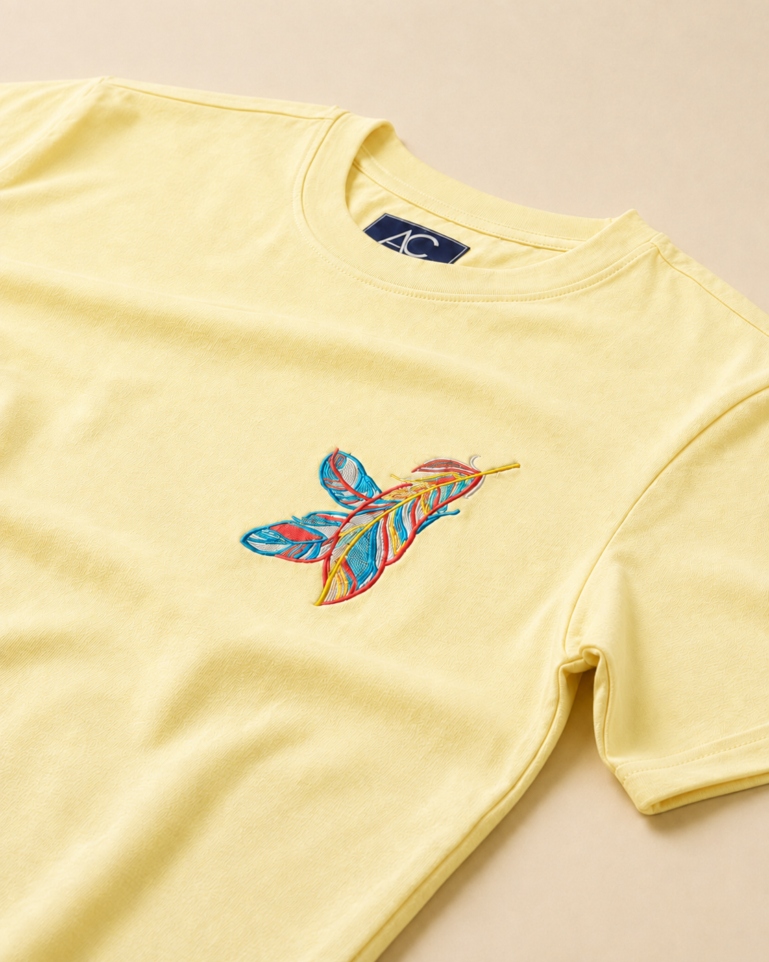 Feather embroidered Cream Regular Fit T-shirt placed on the Light Beige Background