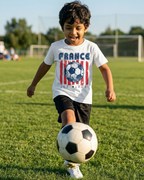 Child wearing a white  t-shirt with 'FRANCE' printed on it in a colourful outdoor playground.