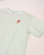 Light green t-shirt with a small ice cream cone design on a pink background