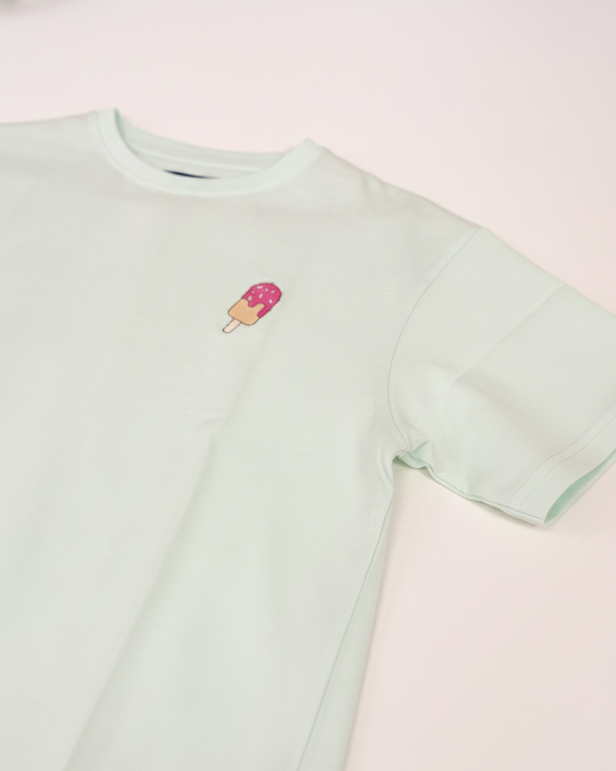 Light green t-shirt with a small ice cream cone design on a pink background