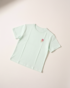 Light green t-shirt with a small red and yellow design on a light pink background